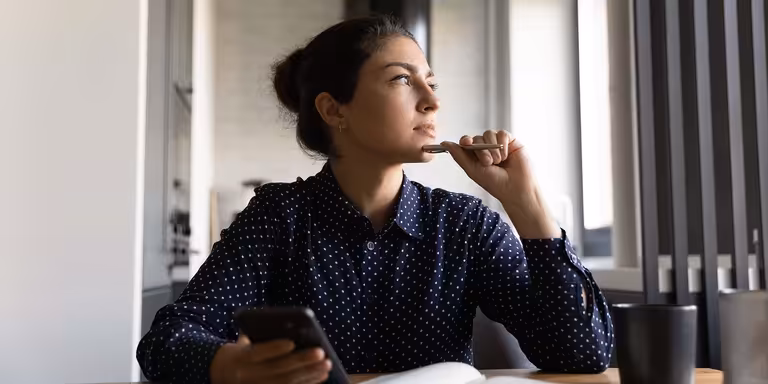 Person considering reasons for applying to a job, phone and pen in hand