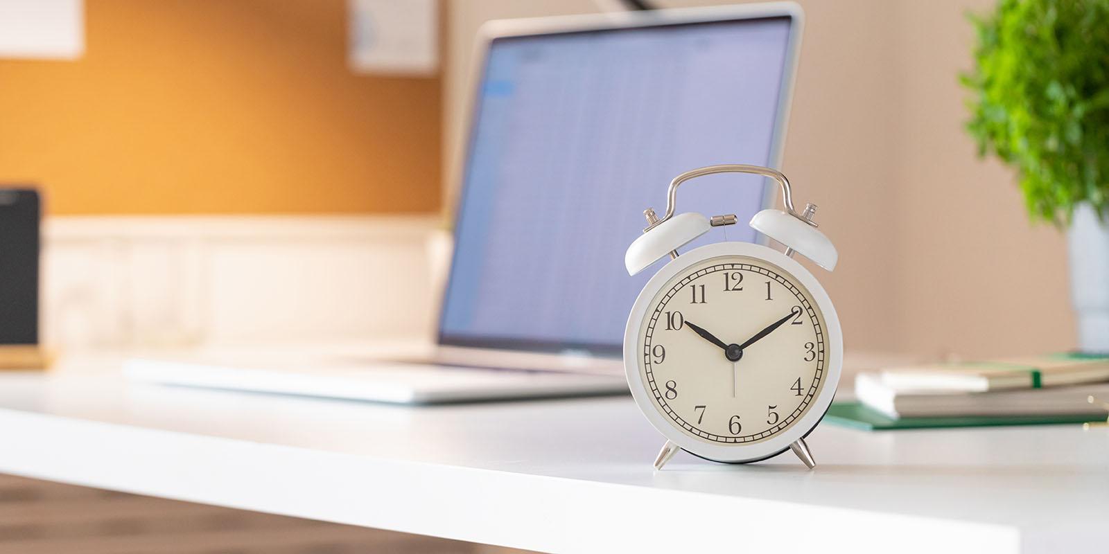 Office with clock and laptop on desk representing part-time or full-time work hours