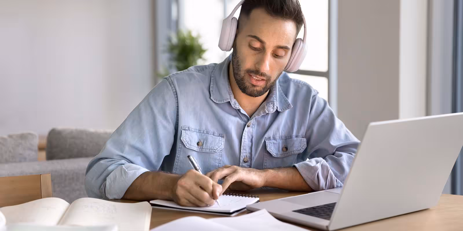 Professional wearing a headset, taking notes in front of a laptop and surrounded by open books for an online course teaching new career skills