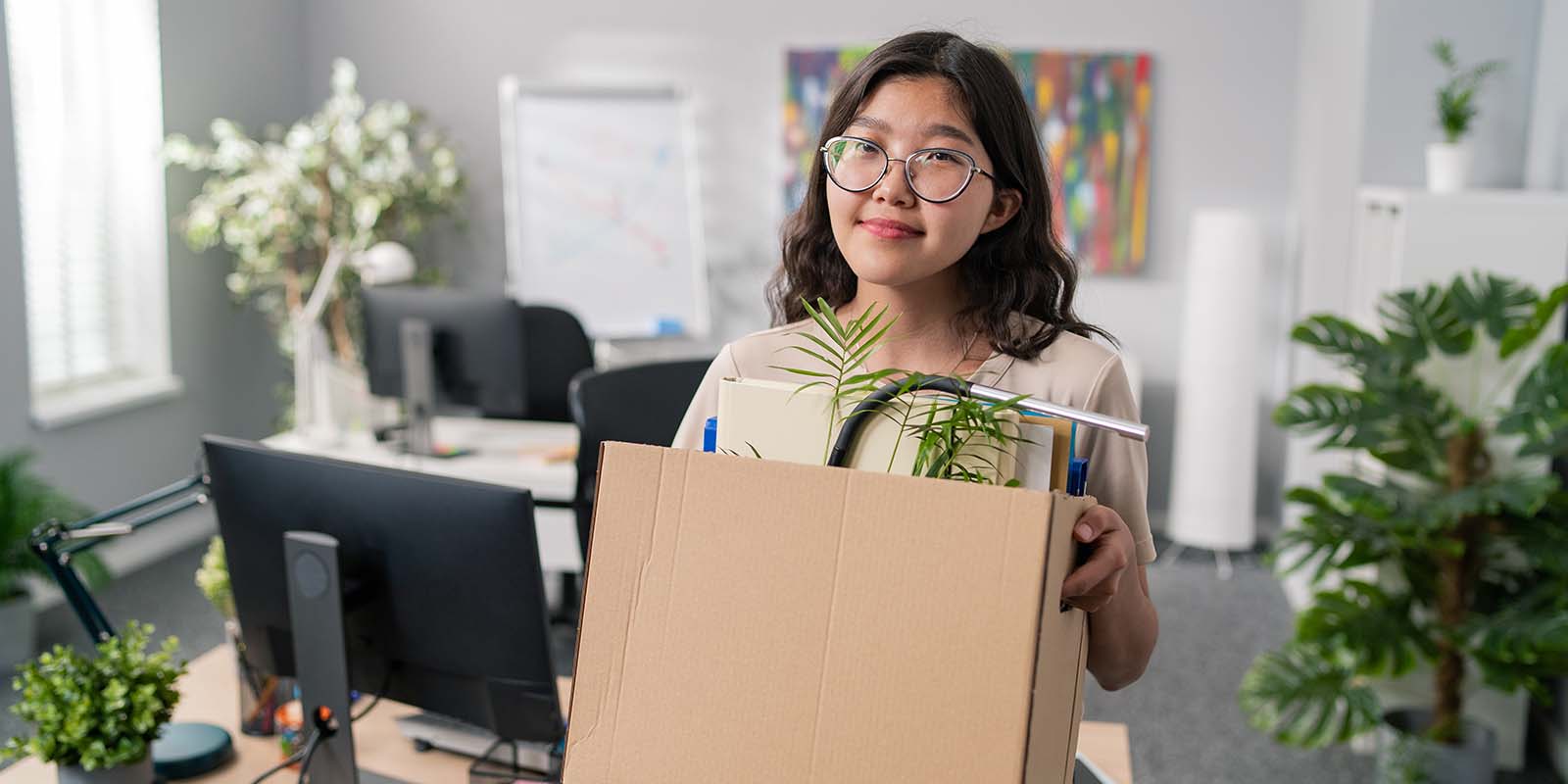 Smiling woman in an office, holding a box of her belongings, leaving her job after quitting