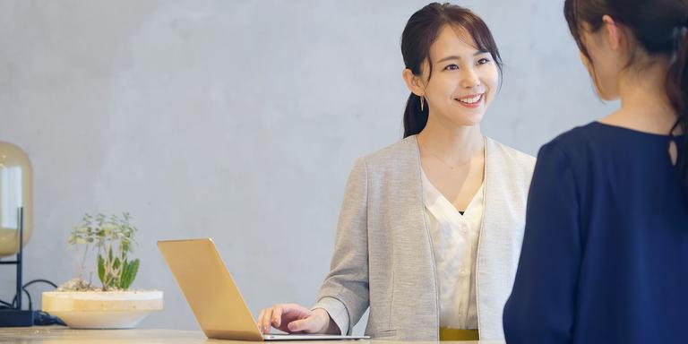 Professional woman smiling and speaking with a customer at a desk with a laptop and plant