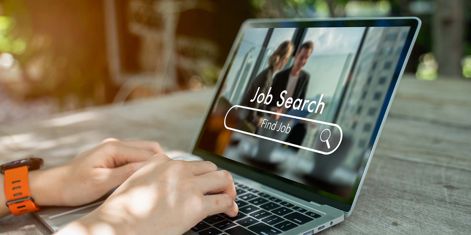 Person typing on a laptop outdoors with a “Job Search – Find Job” screen displayed, showing a search bar and magnifying glass icon