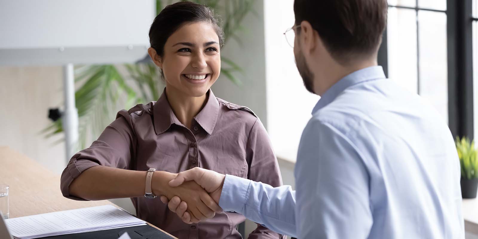 Job candidate at a job interview smiling while shaking hands with the interviewer, representing someone getting hired for a job with no experience.